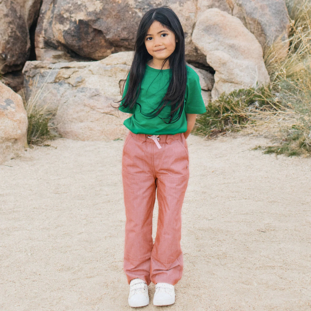 Girl wearing Jackalo Jules chambray pants and green shirt outdoors, sustainable kids fashion