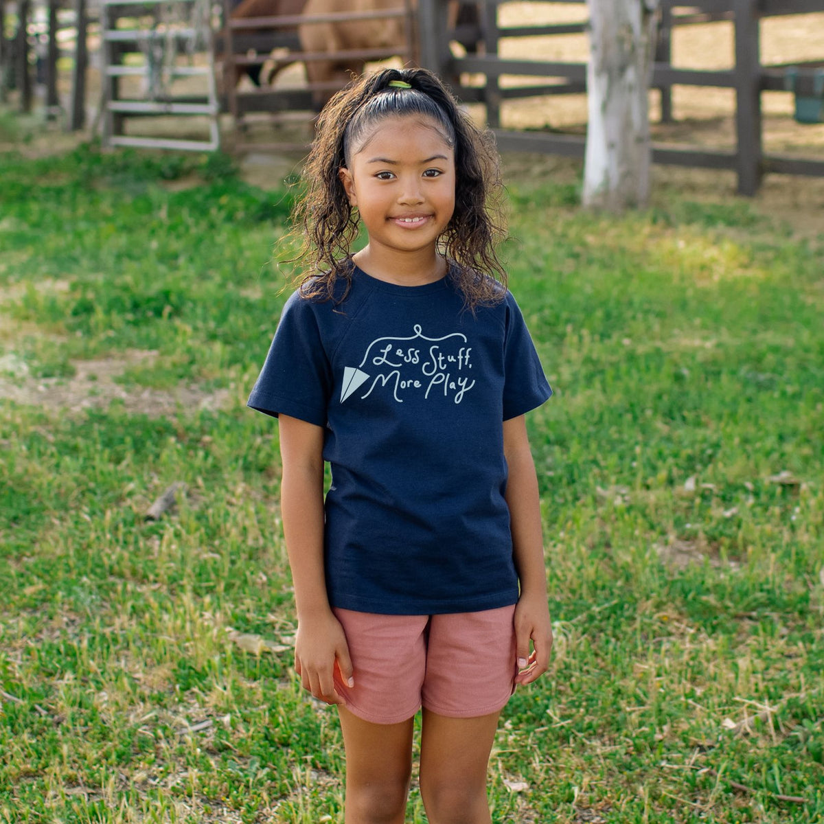 Girl wearing navy shirt that says Less Stuff More Play