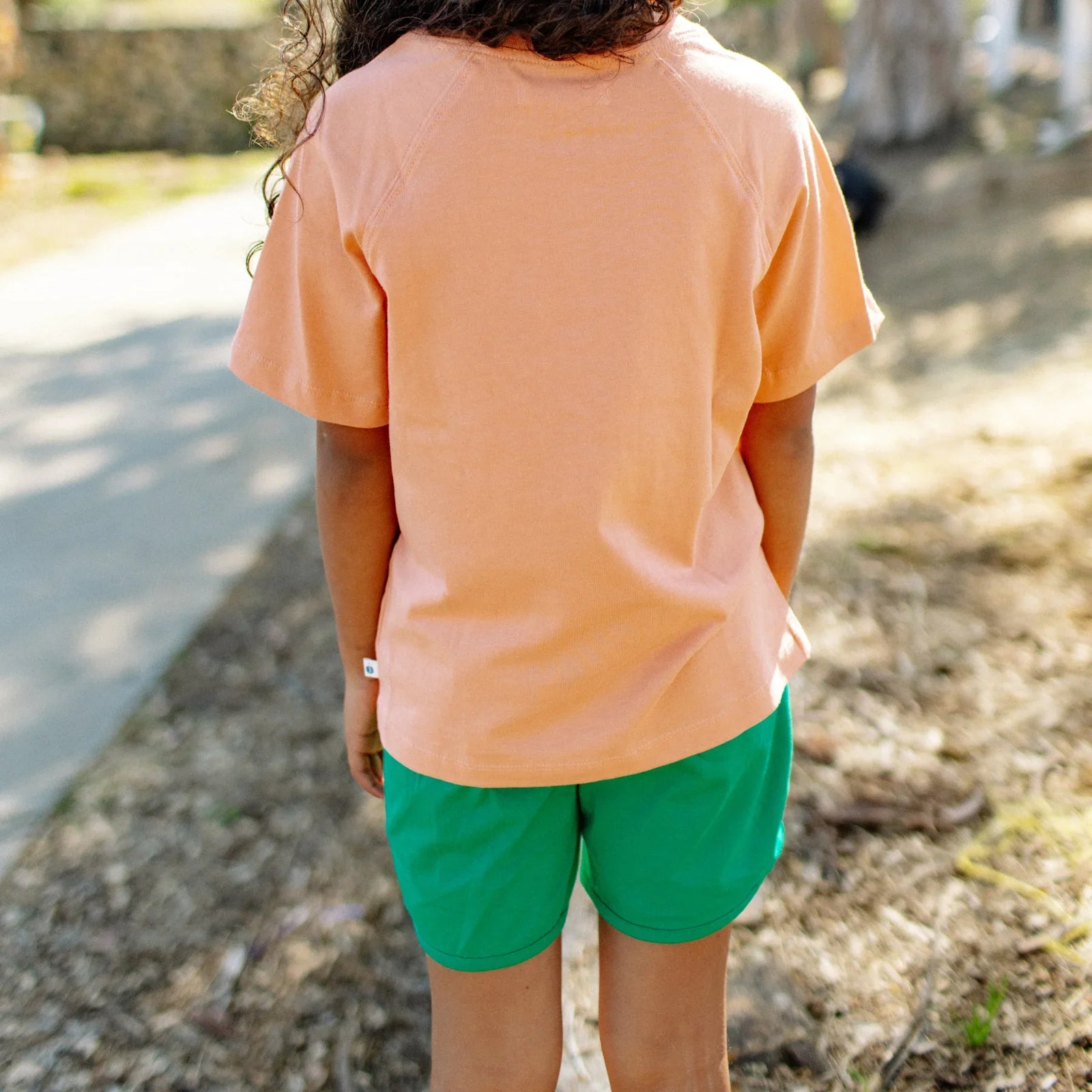 Child in Jackalo sustainable orange shirt and green shorts outdoors on a sunny day