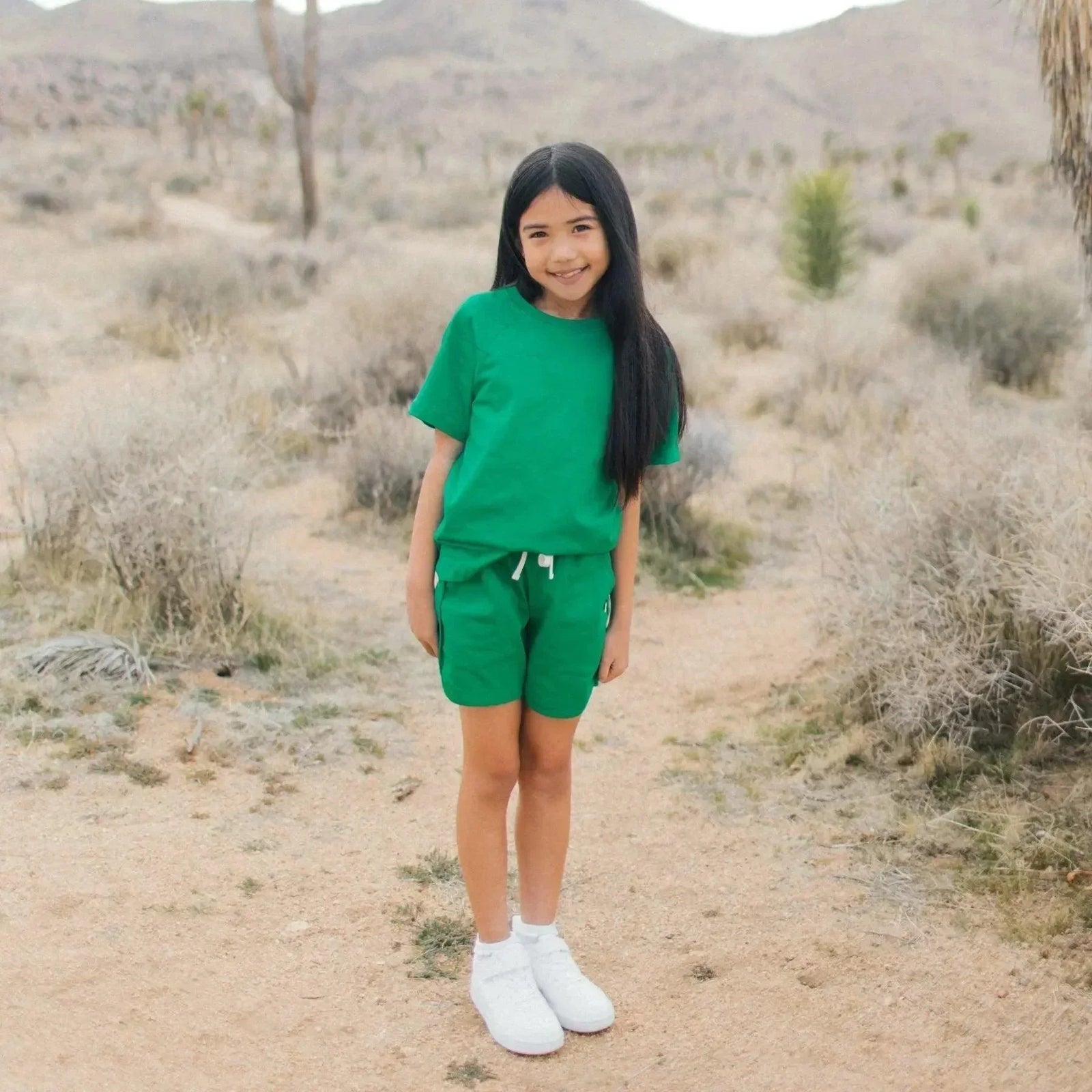 Smiling girl in green Jackalo shorts and t-shirt, standing outdoors in a desert landscape