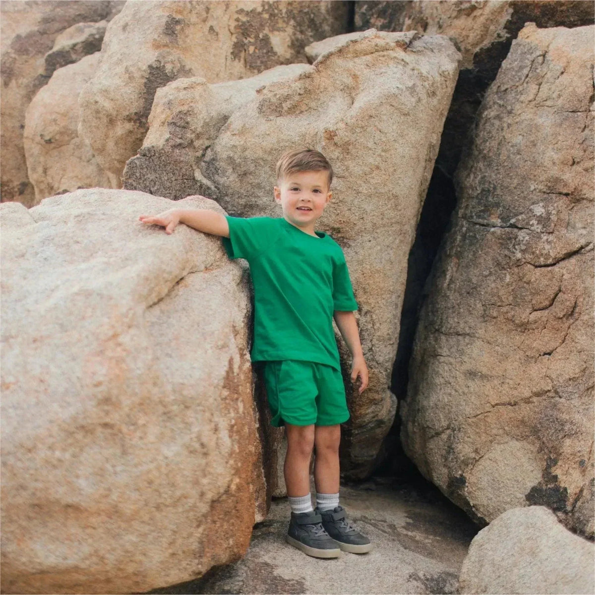 Young boy in green Jackalo shorts and t-shirt standing among large outdoor rocks