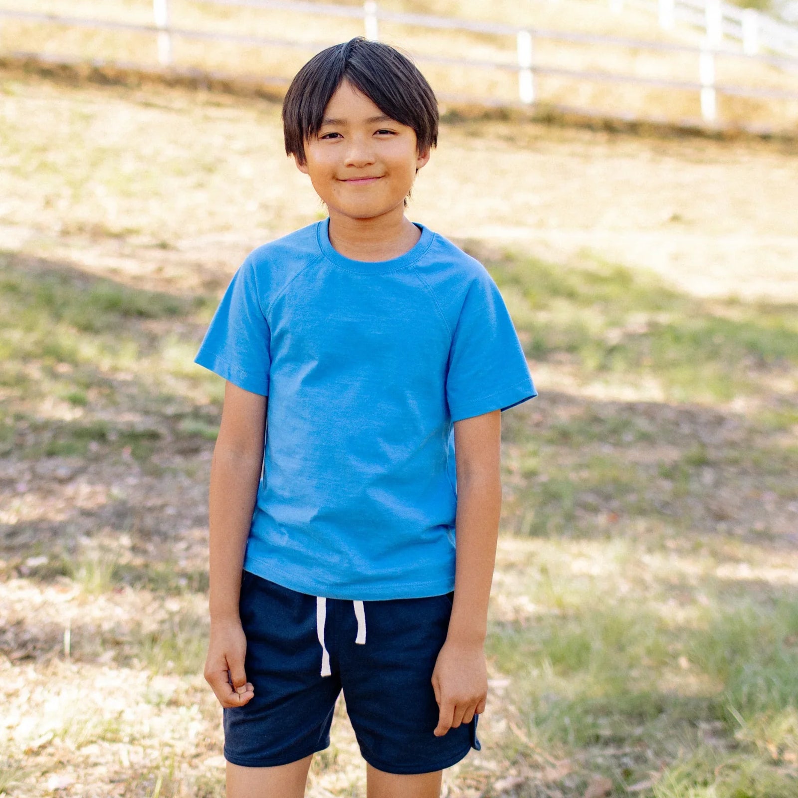 Smiling kid outdoors wearing Jackalo navy shorts and blue t-shirt, sustainable kids clothing