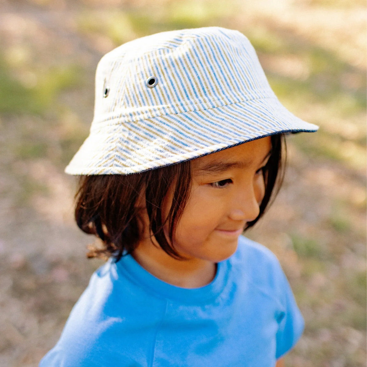 Child wearing Jackalo reversible striped bucket hat and blue shirt outdoors