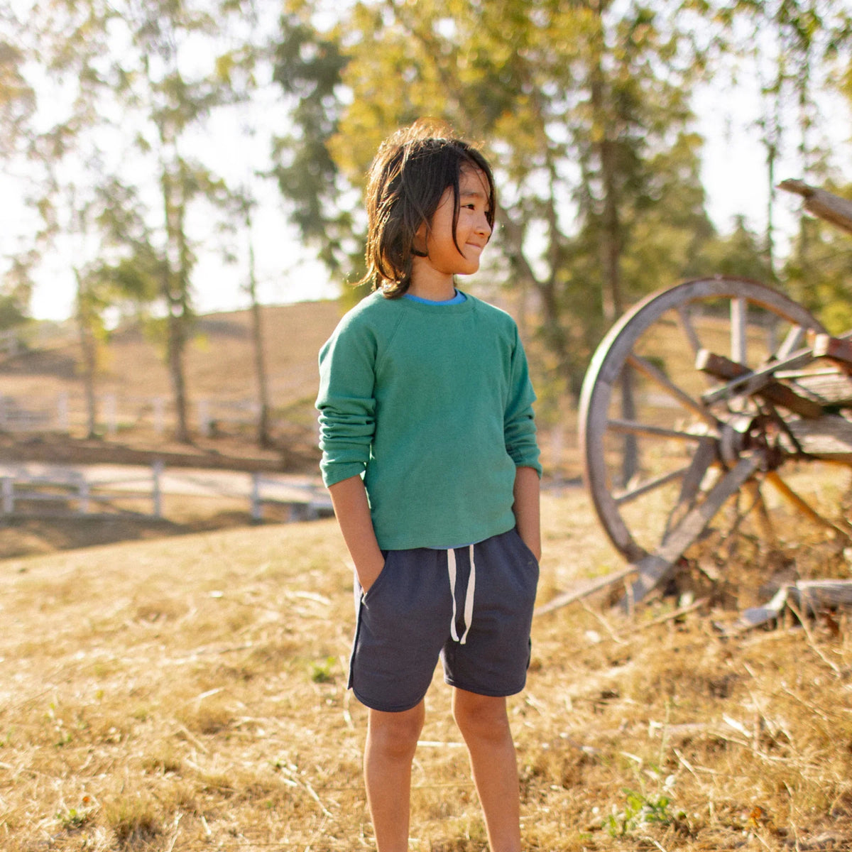 Child in sustainable Jackalo kids' clothes outdoors, wearing green sweatshirt and navy shorts