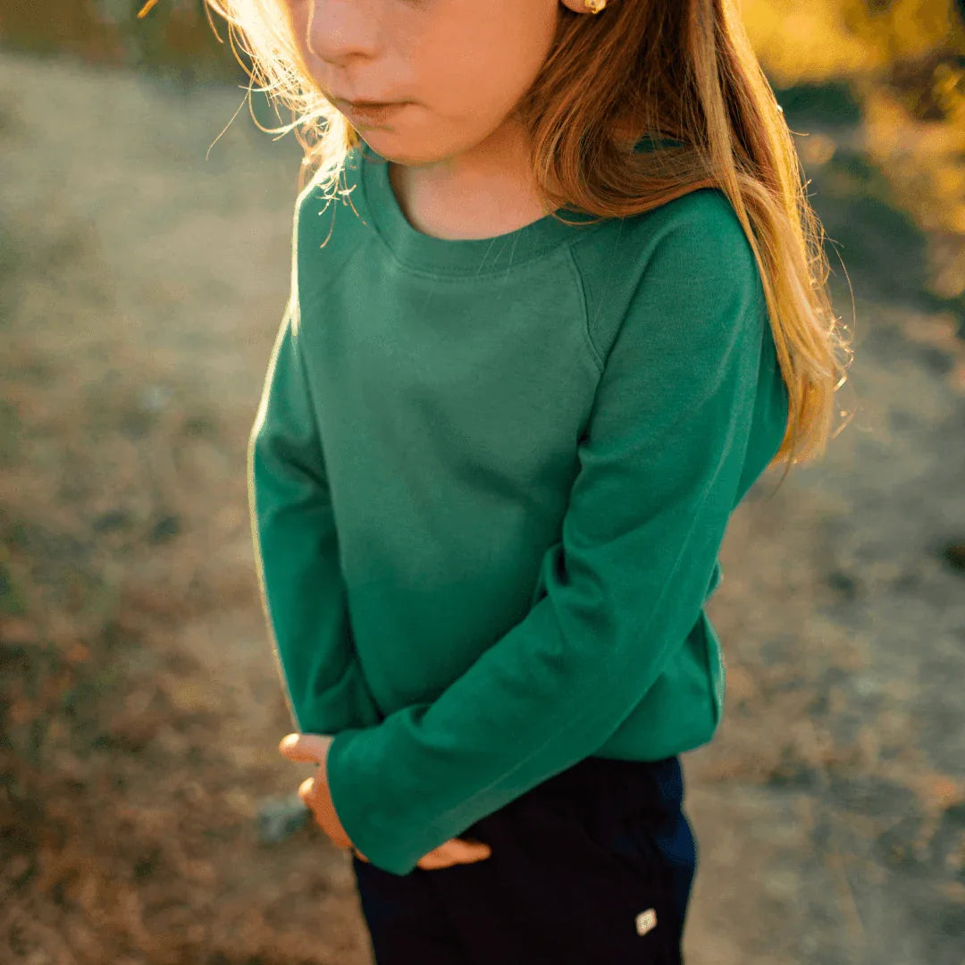 Child wearing sustainable green long sleeve shirt by Jackalo outdoors on a sunny day