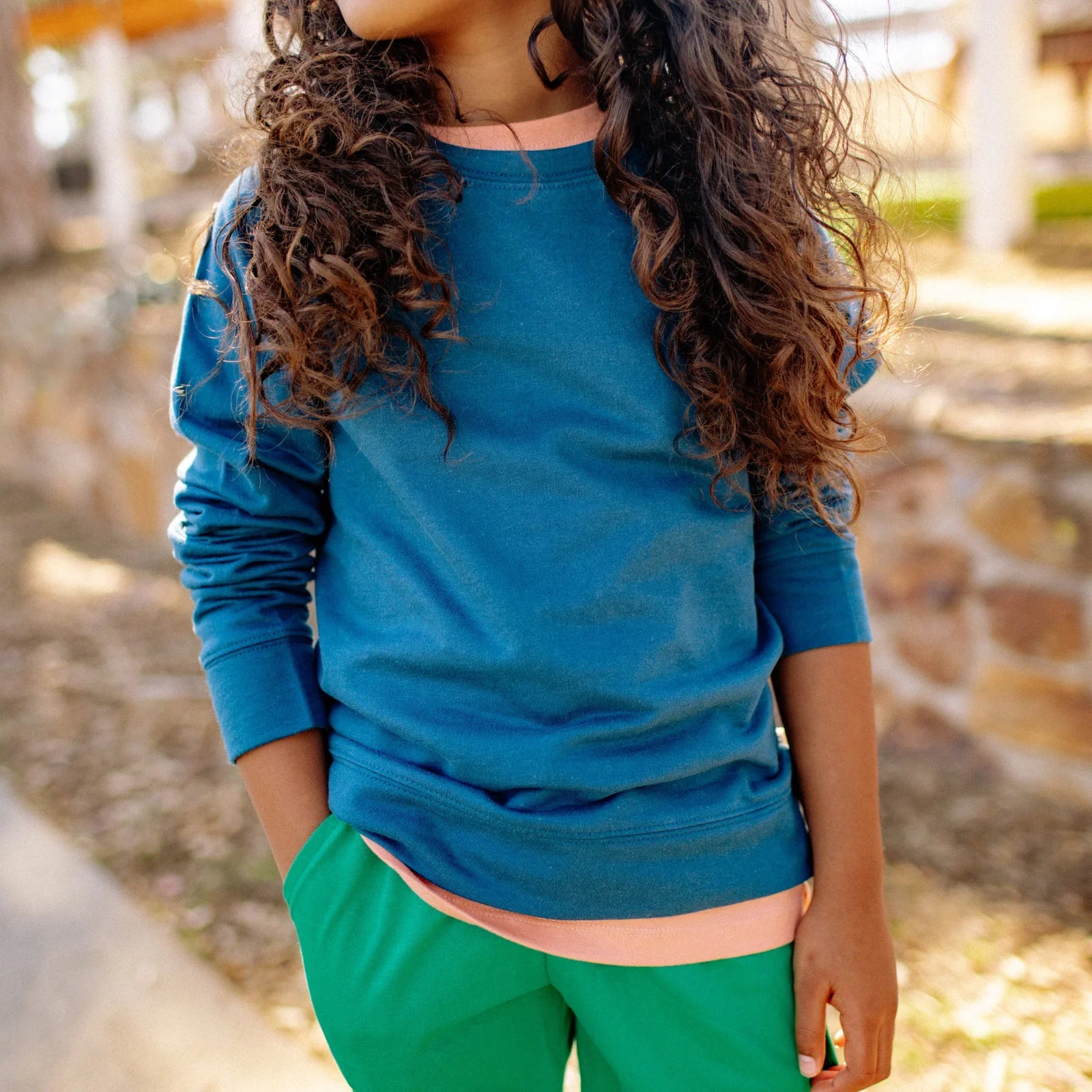 Child wearing Jackalo sustainable blue long-sleeve shirt and green pants outdoors