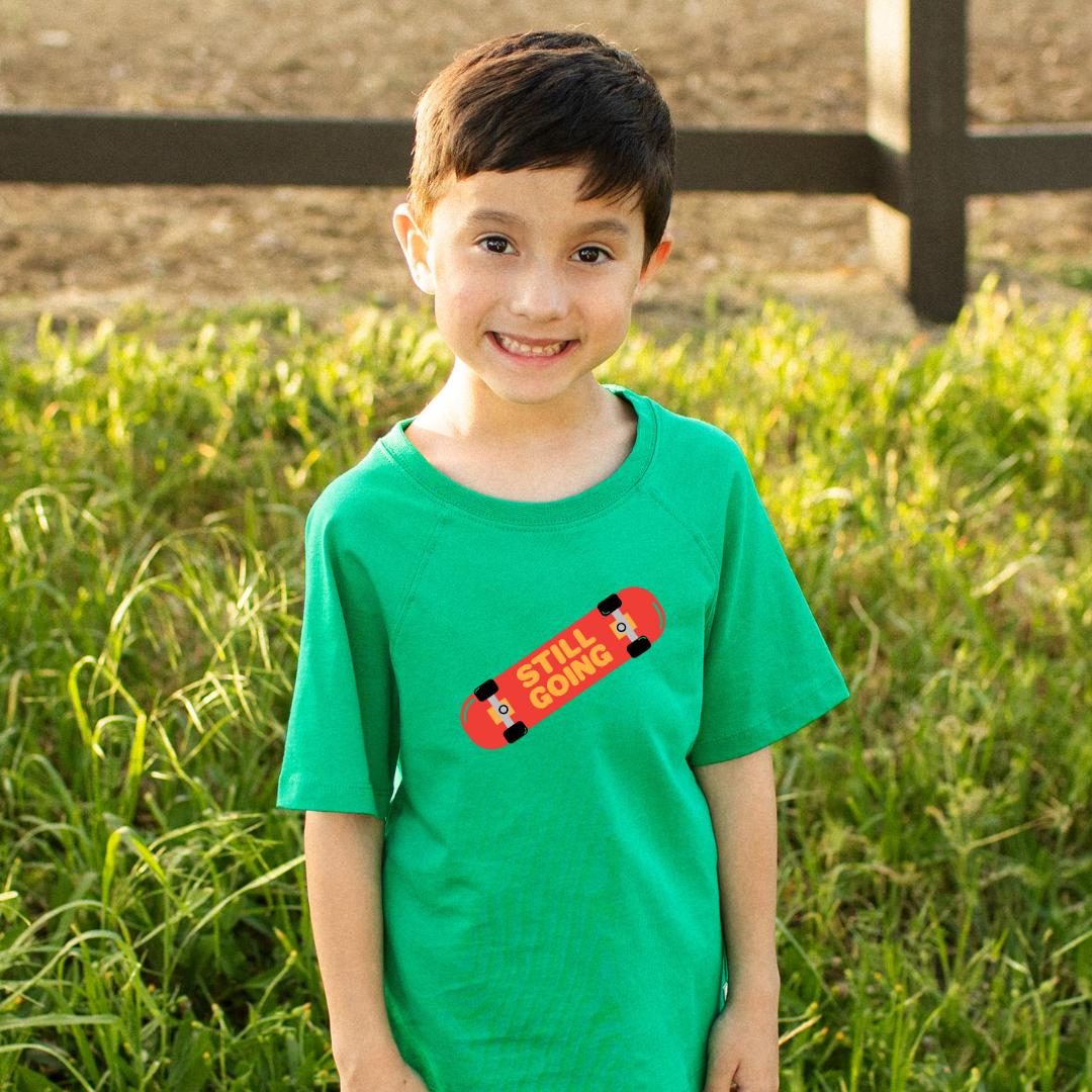 Red skateboard with "still going" graphic on green t-shirt