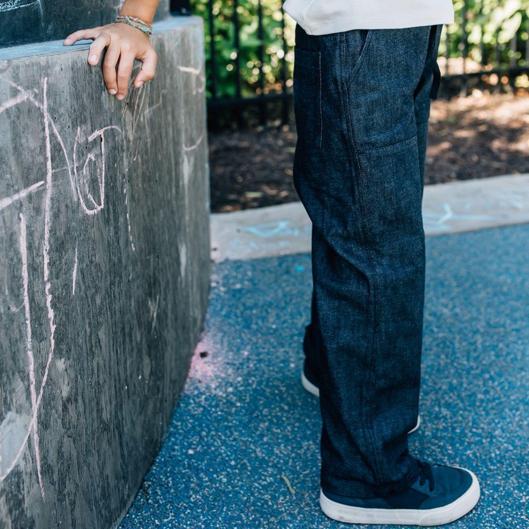 Child wearing Jackalo sustainable jeans, standing by chalk-covered wall outdoors
