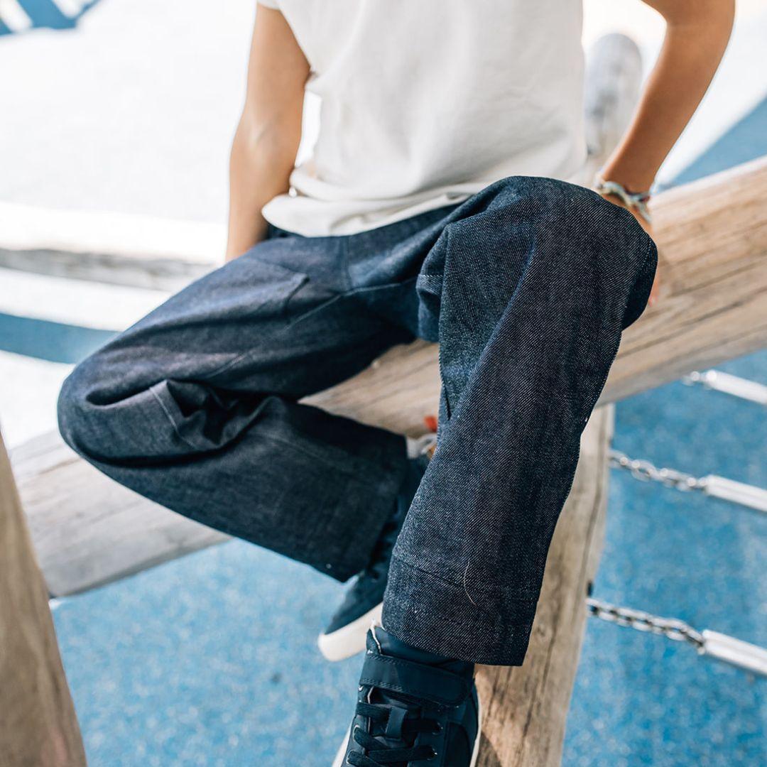 Active kid in dark sustainable Jackalo jeans and sneakers sitting on playground equipment