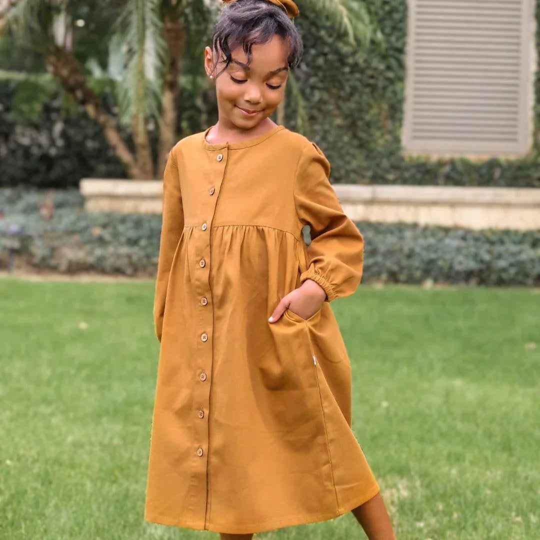 Girl wearing long-sleeved acorn Jo dress by Jackalo, standing on grass outdoors