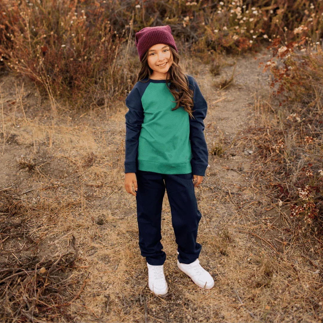 Smiling child in a green and navy raglan shirt, navy pants, and maroon beanie outdoors, Jackalo kidswear