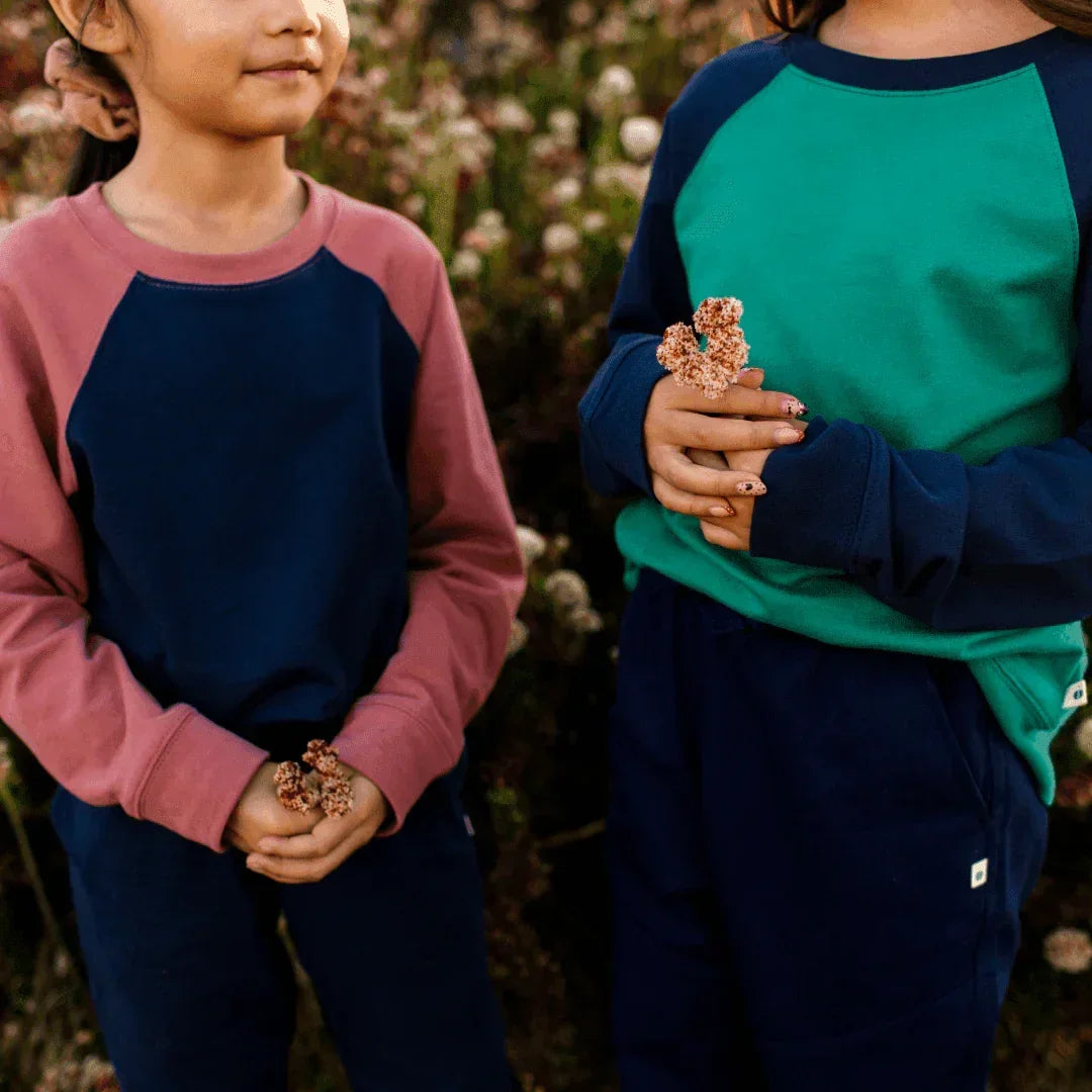 Two kids in Jackalo sustainable raglan sweatshirts, navy and rose, outdoors holding flowers