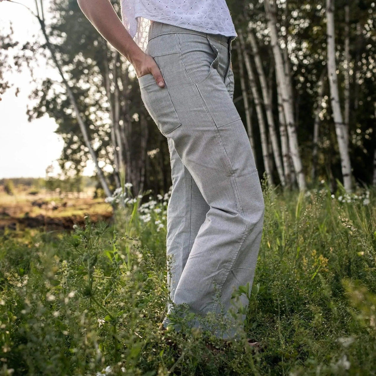 Woman wearing Jackalo Charlie pants outdoors in a grassy field near trees, sustainable clothing